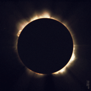 An image of a solar eclipse. A large black circle obscures the sun. Light spills from the edges into black darkness.
