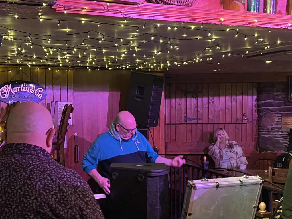 A white man playing air guitar mid way through singing AC/DC at karaoke. 