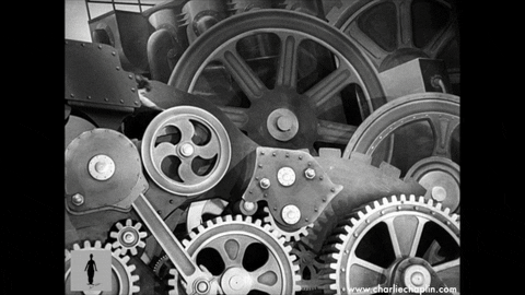 black and white animation of moving cogs, with Charlie Chaplin (the white silent film actor) riding one of the cogs with a spanner in his hand.