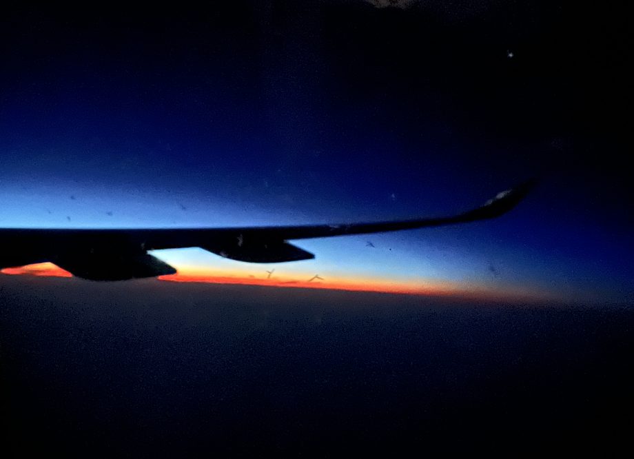 A photo of the wing of a plane with a dark sky and vague sunset on the horizon.